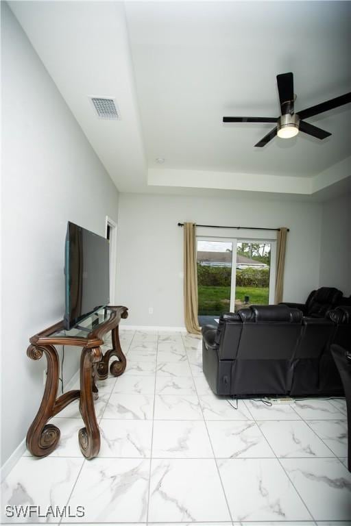living room featuring ceiling fan and a raised ceiling