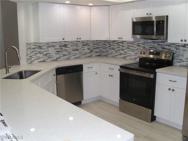 kitchen featuring stainless steel appliances, backsplash, white cabinetry, a sink, and light stone countertops