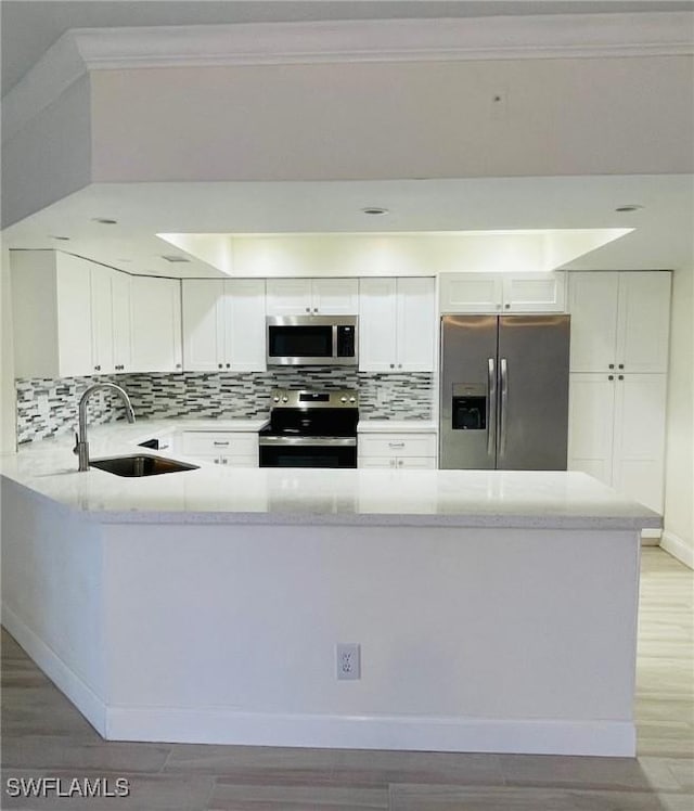 kitchen featuring light wood finished floors, a peninsula, a sink, stainless steel appliances, and backsplash