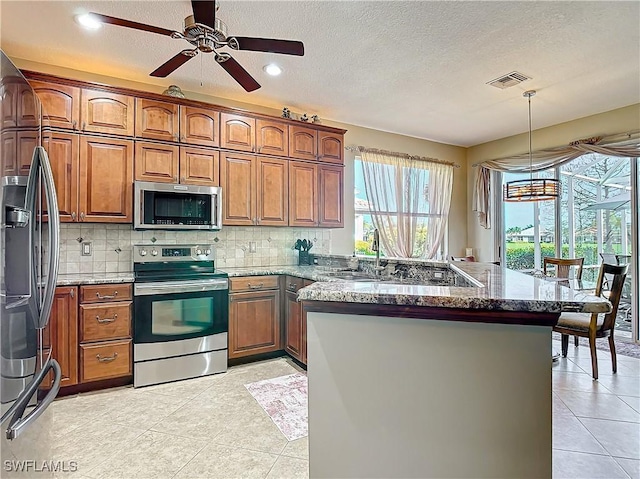 kitchen with hanging light fixtures, dark stone countertops, light tile patterned floors, and stainless steel appliances