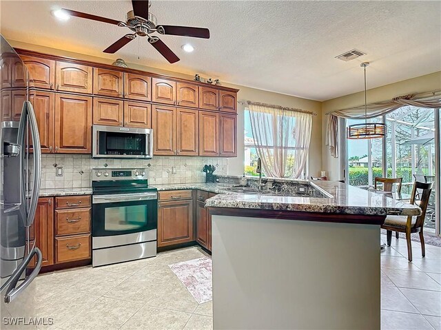 20790 Athenian Ln, North Fort Myers, FL 33917 - kitchen featuring brown cabinetry, visible vents, a peninsula, stainless steel appliances, and dark stone counters