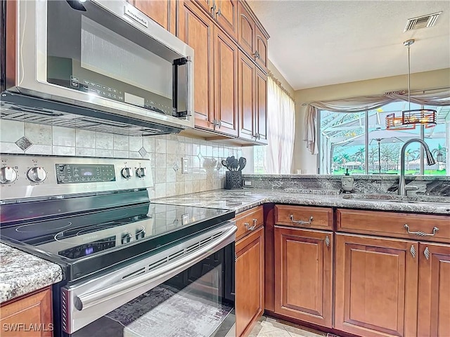 kitchen featuring stainless steel appliances, sink, backsplash, light stone counters, and pendant lighting