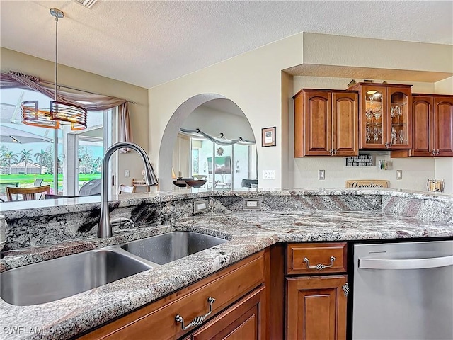 kitchen featuring light stone countertops, sink, stainless steel dishwasher, a textured ceiling, and pendant lighting