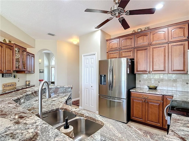 kitchen featuring electric range, stainless steel fridge, sink, backsplash, and light stone counters