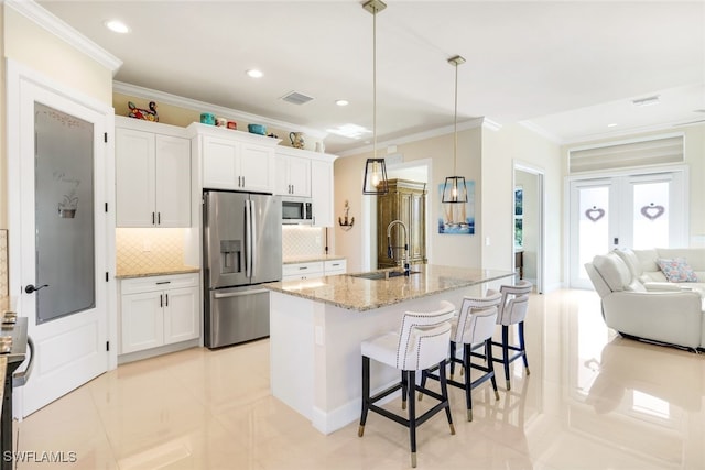 kitchen with a breakfast bar, white cabinetry, hanging light fixtures, a center island with sink, and appliances with stainless steel finishes