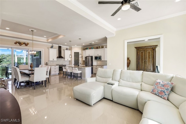 living room with ornamental molding, sink, ceiling fan with notable chandelier, and a tray ceiling