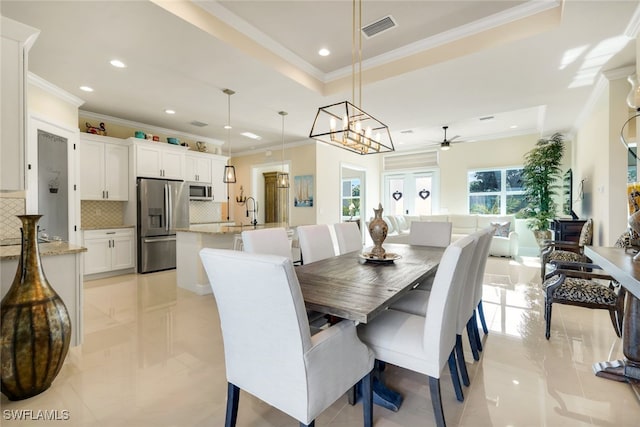 dining room with a raised ceiling, crown molding, sink, and ceiling fan with notable chandelier