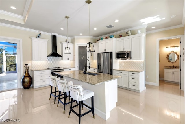 kitchen featuring sink, white cabinets, wall chimney range hood, stainless steel appliances, and a center island with sink