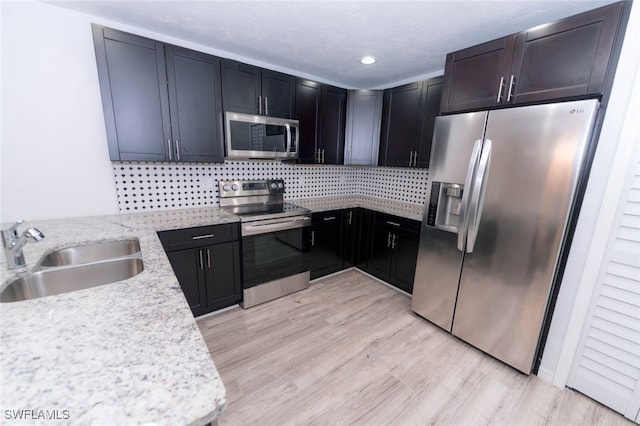 kitchen featuring appliances with stainless steel finishes, sink, decorative backsplash, light stone countertops, and light wood-type flooring