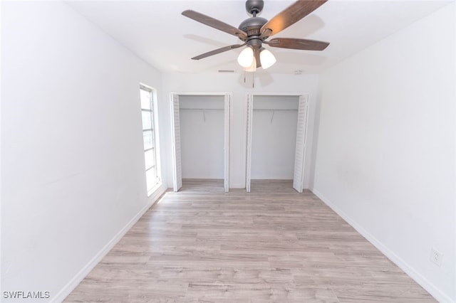 unfurnished bedroom featuring ceiling fan, two closets, and light wood-type flooring