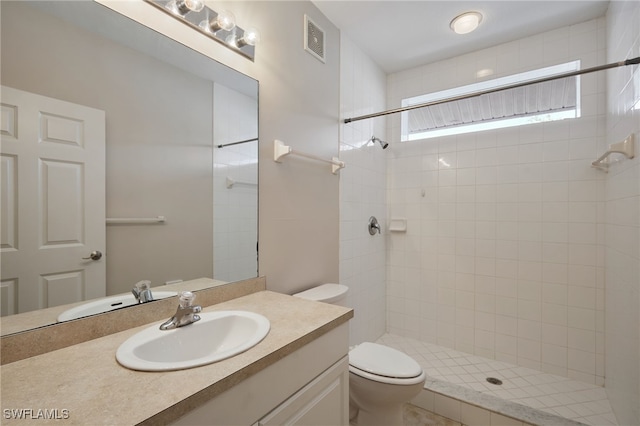 bathroom featuring toilet, visible vents, a tile shower, and vanity