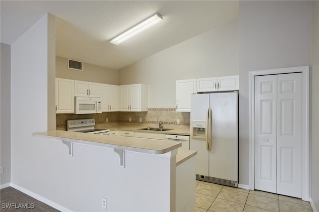 kitchen with a breakfast bar area, a peninsula, white appliances, a sink, and white cabinets