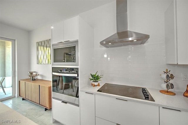 kitchen featuring built in microwave, white cabinets, stainless steel oven, black electric cooktop, and wall chimney exhaust hood