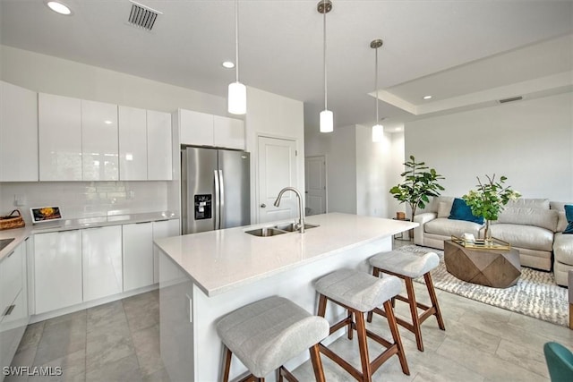 kitchen with white cabinetry, an island with sink, sink, a breakfast bar area, and stainless steel refrigerator with ice dispenser