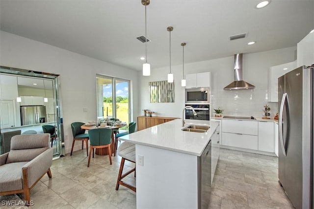 kitchen with wall chimney exhaust hood, an island with sink, pendant lighting, stainless steel appliances, and white cabinets