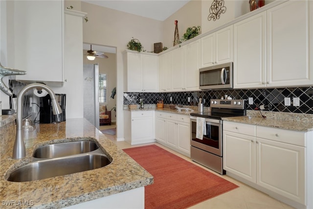 kitchen featuring sink, light stone counters, appliances with stainless steel finishes, white cabinets, and decorative backsplash