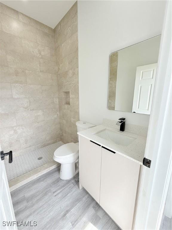 bathroom featuring vanity, hardwood / wood-style floors, toilet, and tiled shower