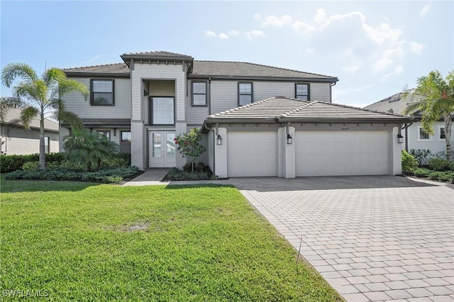 view of front of property featuring an attached garage, a tile roof, decorative driveway, and a front lawn