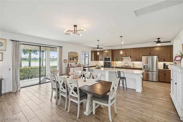 dining space featuring visible vents, ceiling fan with notable chandelier, a water view, and light wood finished floors