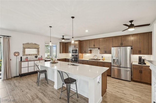 kitchen featuring light wood-style flooring, stainless steel appliances, light countertops, under cabinet range hood, and backsplash