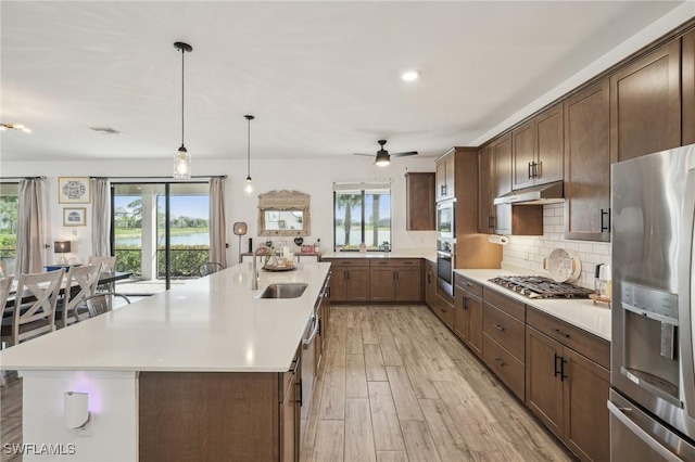 kitchen with under cabinet range hood, light countertops, decorative backsplash, stainless steel appliances, and a sink