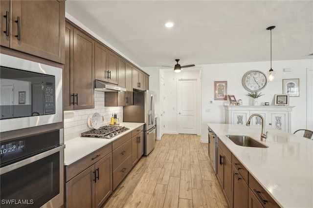 kitchen with a sink, decorative backsplash, light countertops, stainless steel appliances, and under cabinet range hood