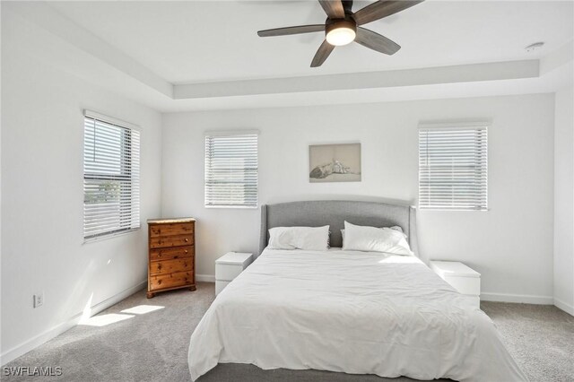 bedroom featuring a raised ceiling, carpet flooring, baseboards, and ceiling fan