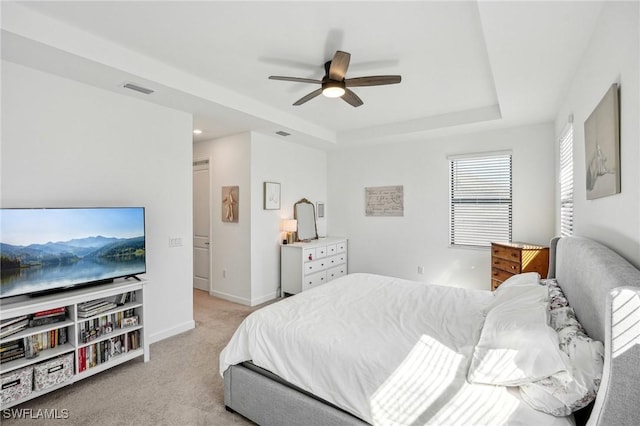 bedroom with visible vents, baseboards, ceiling fan, light colored carpet, and a tray ceiling