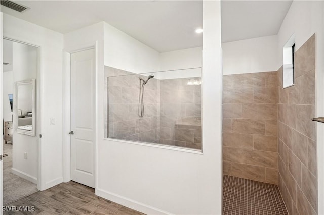 full bathroom with wood finished floors, visible vents, a tile shower, and baseboards