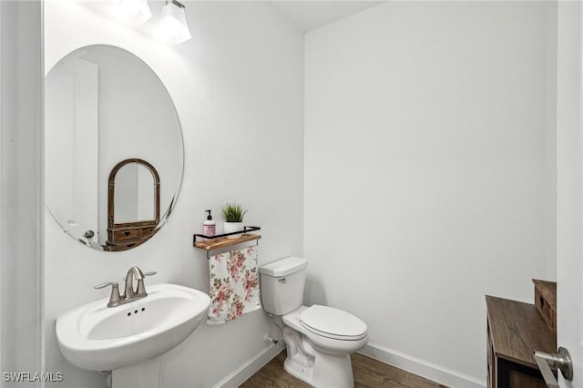 half bath featuring toilet, wood finished floors, baseboards, and a sink