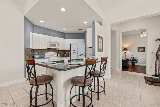 kitchen with white appliances, tasteful backsplash, light tile patterned floors, white cabinets, and a breakfast bar