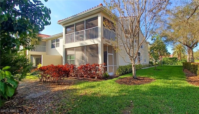 rear view of house with a sunroom, a lawn, and stucco siding