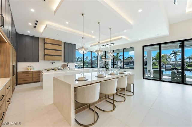 kitchen featuring a raised ceiling, a large island, modern cabinets, light countertops, and a sink