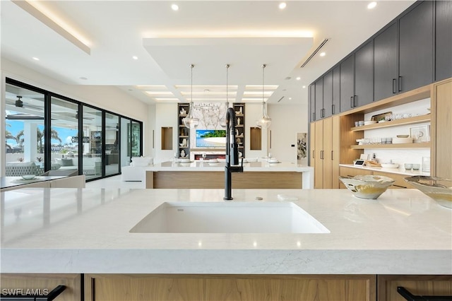 kitchen featuring open shelves, recessed lighting, a sink, light stone countertops, and dark cabinets