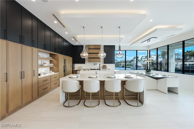 kitchen with a spacious island, a kitchen breakfast bar, a tray ceiling, light countertops, and dark cabinetry