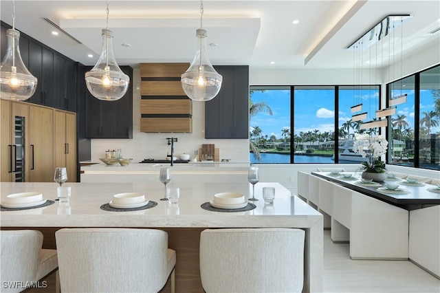 kitchen with a kitchen island with sink, recessed lighting, dark cabinets, a breakfast bar, and hanging light fixtures