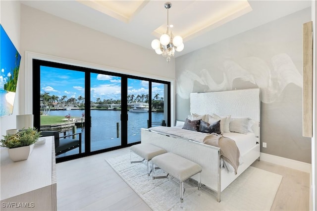 bedroom featuring a notable chandelier, a water view, wood finished floors, baseboards, and access to exterior