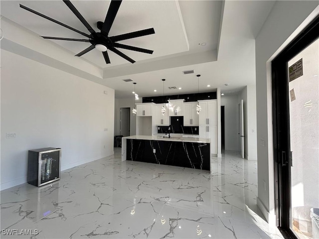 unfurnished living room featuring a sink, visible vents, baseboards, marble finish floor, and a raised ceiling