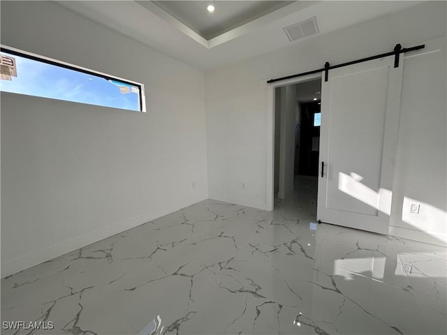 unfurnished room featuring marble finish floor, a barn door, visible vents, and baseboards