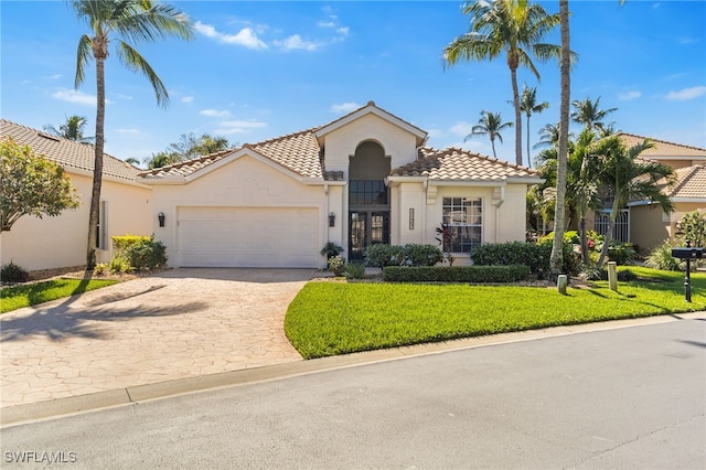 mediterranean / spanish-style house featuring an attached garage, a tile roof, a front yard, and stucco siding