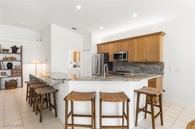 kitchen with light stone counters, brown cabinets, backsplash, appliances with stainless steel finishes, and washer and dryer