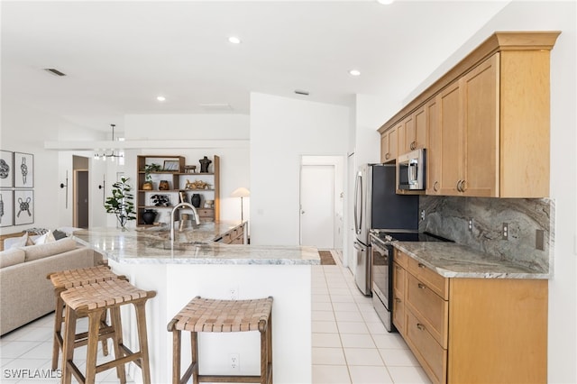 kitchen with backsplash, appliances with stainless steel finishes, open floor plan, light tile patterned flooring, and a kitchen bar