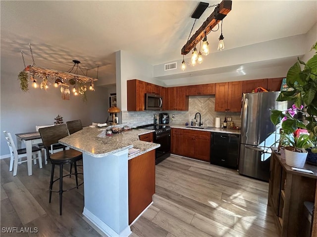 kitchen featuring sink, a breakfast bar area, kitchen peninsula, pendant lighting, and black appliances