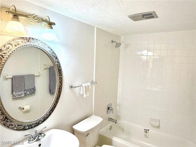 full bathroom featuring toilet, tiled shower / bath combo, sink, and a textured ceiling