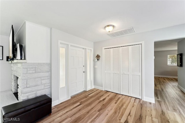 foyer entrance featuring light wood-style floors, baseboards, a fireplace, and visible vents