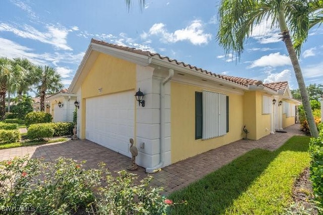 view of side of home with a garage, a tile roof, and stucco siding