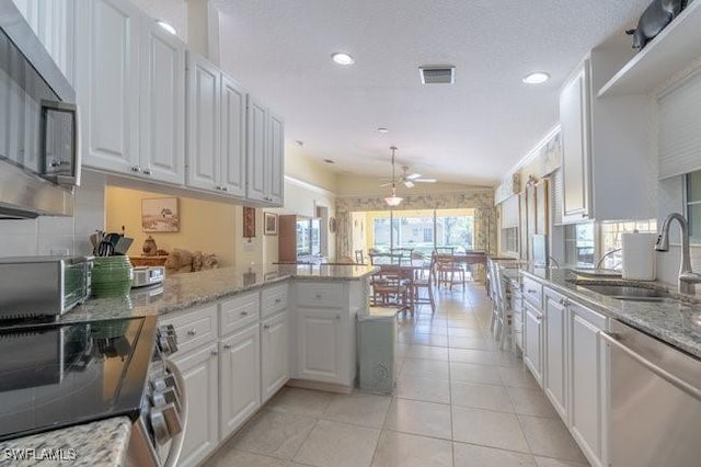 kitchen with a ceiling fan, a peninsula, a sink, stainless steel appliances, and white cabinetry