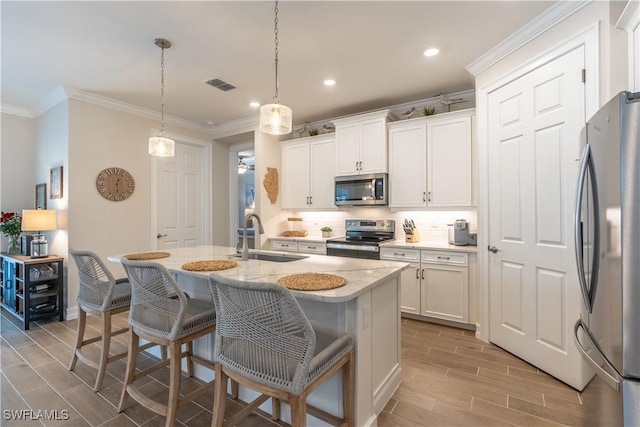 kitchen featuring white cabinets, pendant lighting, stainless steel appliances, a kitchen island with sink, and sink