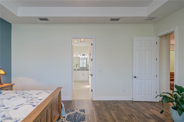 bedroom with a raised ceiling, visible vents, dark wood finished floors, and baseboards