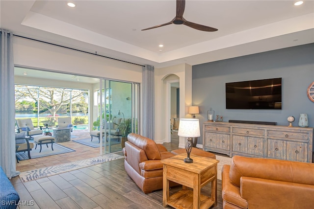 living room featuring wood finished floors, a raised ceiling, a ceiling fan, and recessed lighting